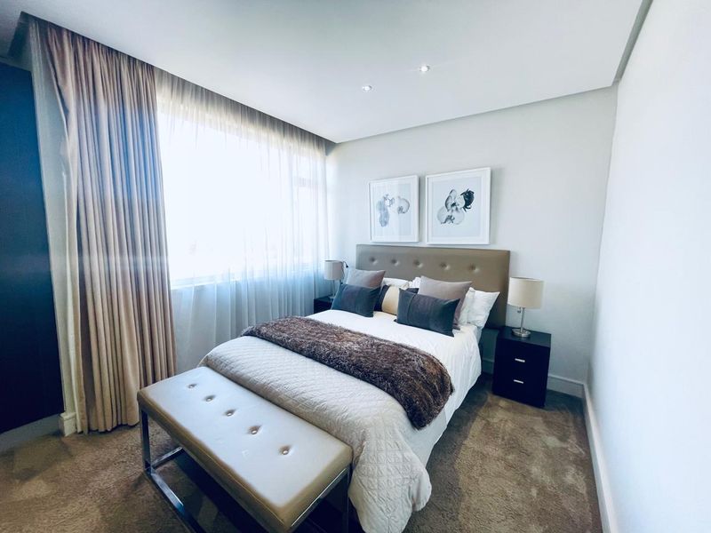 A well-maintained bedroom featuring neutral carpeted flooring, recessed downlighting, and floor-to-ceiling window treatments.