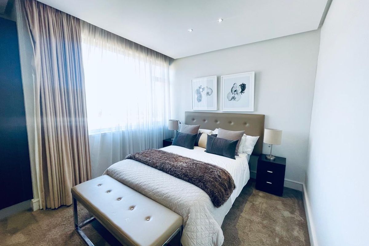 A well-maintained bedroom featuring neutral carpeted flooring, recessed downlighting, and floor-to-ceiling window treatments.