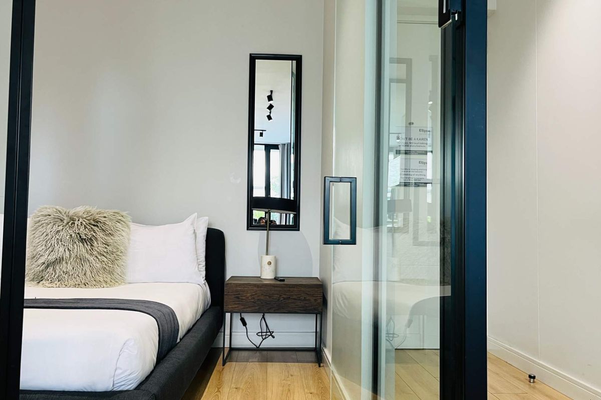 A modern bedroom featuring light wood flooring and a contemporary glass partition wall with a black frame.