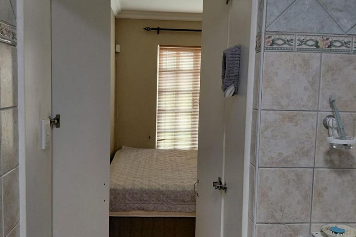 View from a tiled bathroom looking through a doorway into an adjacent bedroom with laminate flooring and window blinds.
