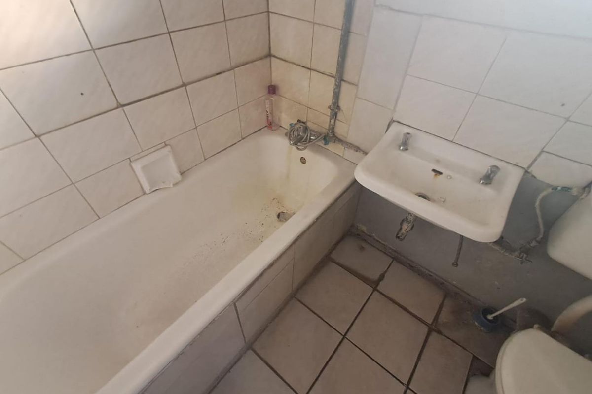 A dated bathroom featuring a standard bathtub, wall-mounted basin, and toilet, requiring significant renovation and modernization of fixtures and finishes.