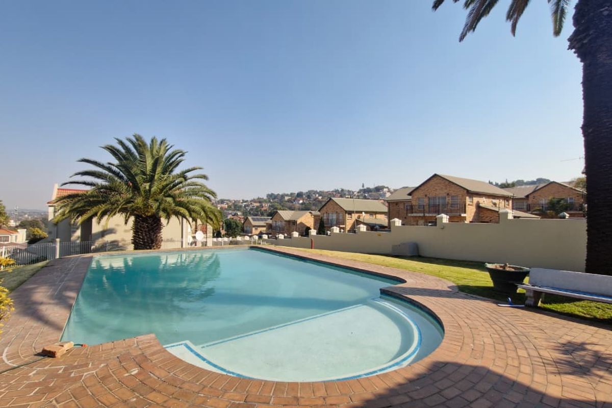 Outdoor swimming pool area featuring brick paving, a perimeter wall, and established palm trees in a residential townhouse setting.
