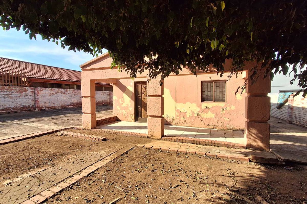 Rear exterior view of a house featuring a covered patio, brick perimeter wall, and significant exterior wall finish deterioration requiring maintenance.