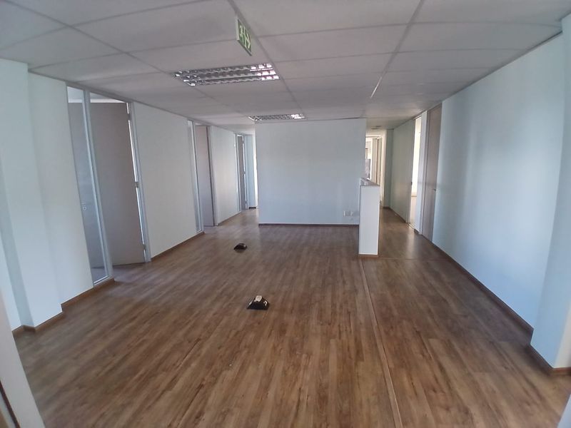 An open-plan office space featuring laminate wood flooring, suspended ceilings with recessed lighting, and multiple internal partition doors.