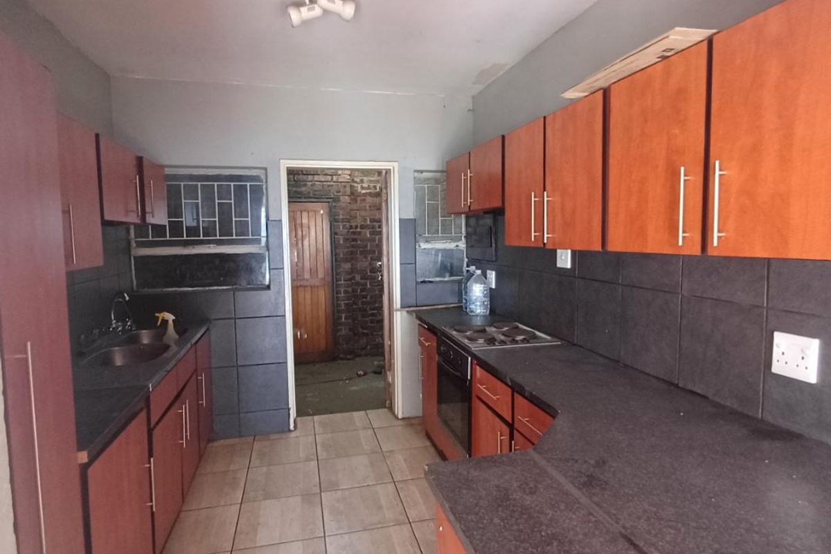 A functional kitchen featuring laminate cabinetry, stone-look countertops, built-in oven and hob, and tiled flooring, requiring some cosmetic updates to improve its overall condition.