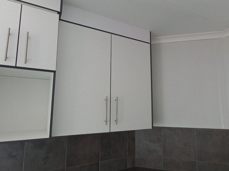 A clean kitchen area featuring modern white built-in cabinetry and dark tiled backsplash.