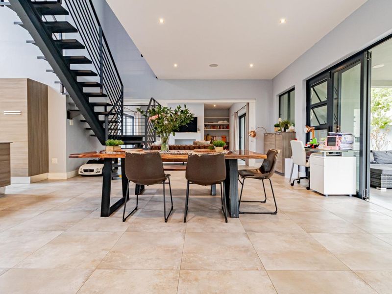 Spacious open-plan living and dining area featuring modern tiled flooring, a striking metal staircase, and large sliding glass doors leading to the patio.