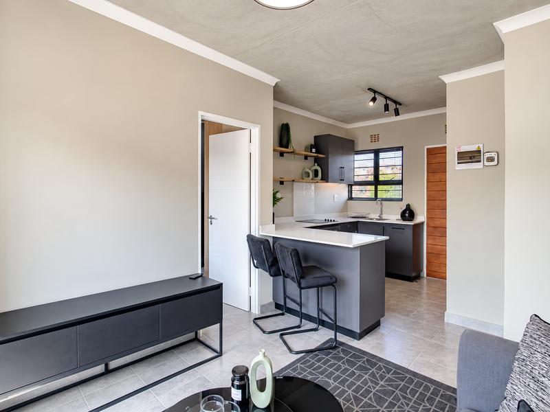 Modern open-plan living area featuring a sleek kitchen with stone countertops, dark cabinetry, and tiled flooring, complemented by an exposed concrete ceiling.