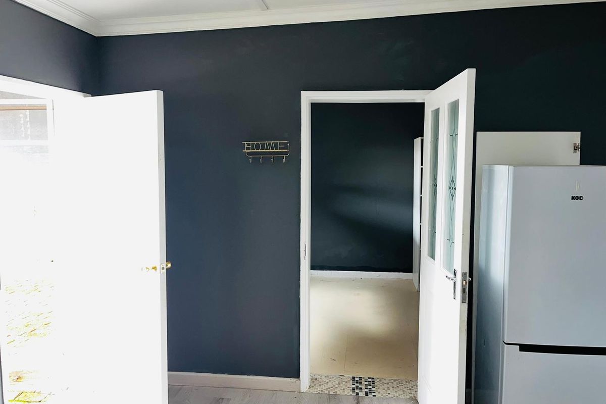 An interior view showing a dark-painted room with a doorway leading to an adjacent space, featuring laminate flooring and white door frames.