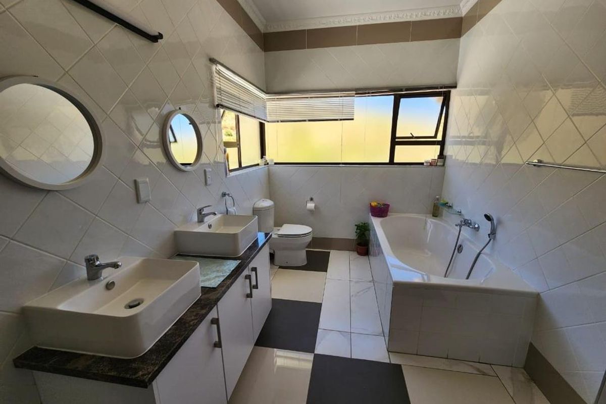 A well-lit bathroom featuring a double vanity with vessel sinks, a built-in bathtub, and modern tiled finishes throughout.