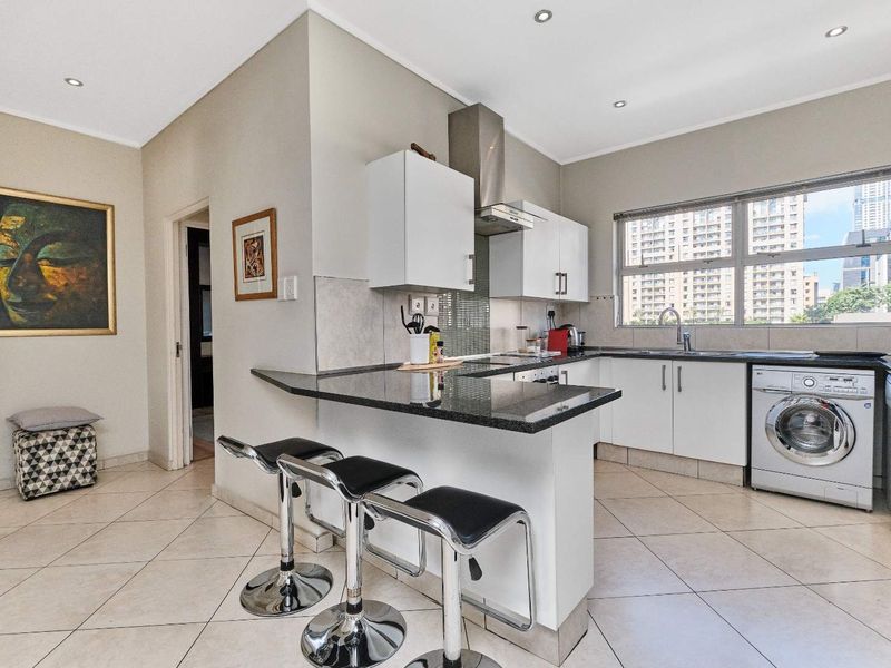 Modern kitchen featuring granite countertops, white cabinetry, stainless steel extractor fan, and integrated laundry facilities, complemented by tiled flooring and recessed lighting.