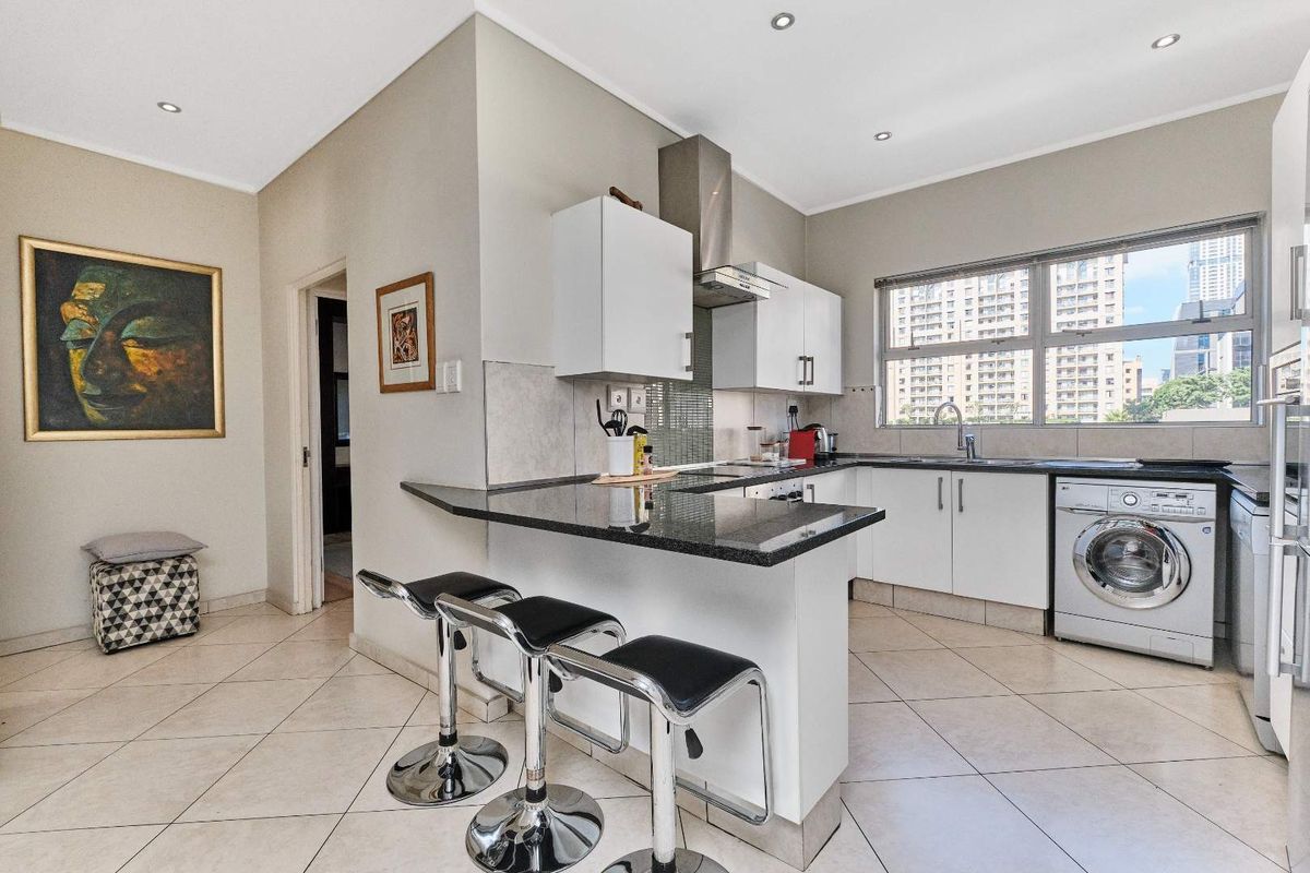 Modern kitchen featuring granite countertops, white cabinetry, stainless steel extractor fan, and integrated laundry facilities, complemented by tiled flooring and recessed lighting.