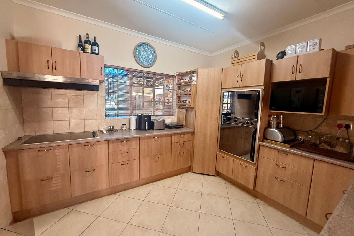 A functional kitchen featuring light wood cabinetry, tiled flooring, a built-in oven, and a glass-top hob with an integrated extractor fan.