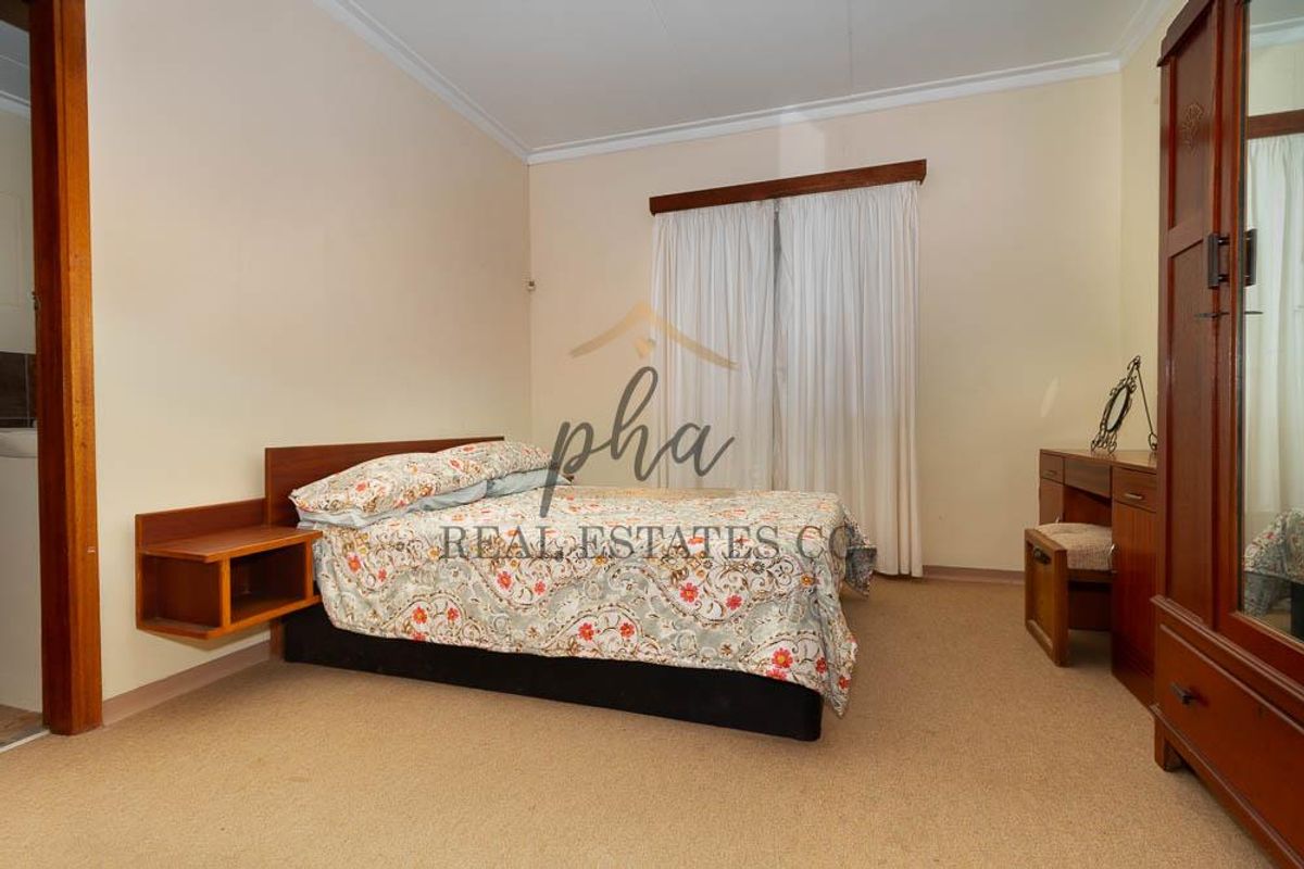 A standard bedroom featuring neutral walls, carpeted flooring, and a built-in wooden headboard with integrated bedside shelving.