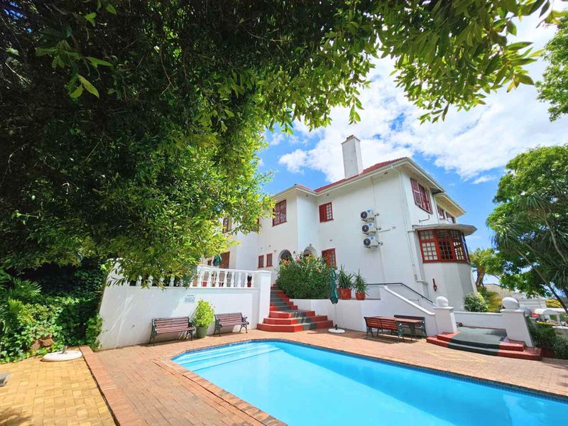 A well-maintained outdoor pool area featuring brick paving, a white balustrade, and a staircase leading to the rear elevation of the multi-story house.