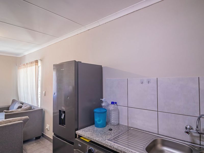 Open plan living area featuring a compact kitchen corner with a stainless steel sink, tiled backsplash, and granite countertop, flowing into the lounge space.