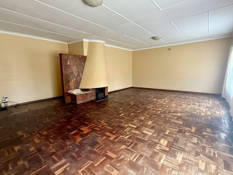 Spacious living room featuring original parquet flooring and a unique built-in stone fireplace, offering a blank canvas for renovation.