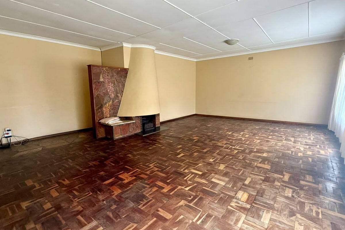 Spacious living room featuring original parquet flooring and a unique built-in stone fireplace, offering a blank canvas for renovation.