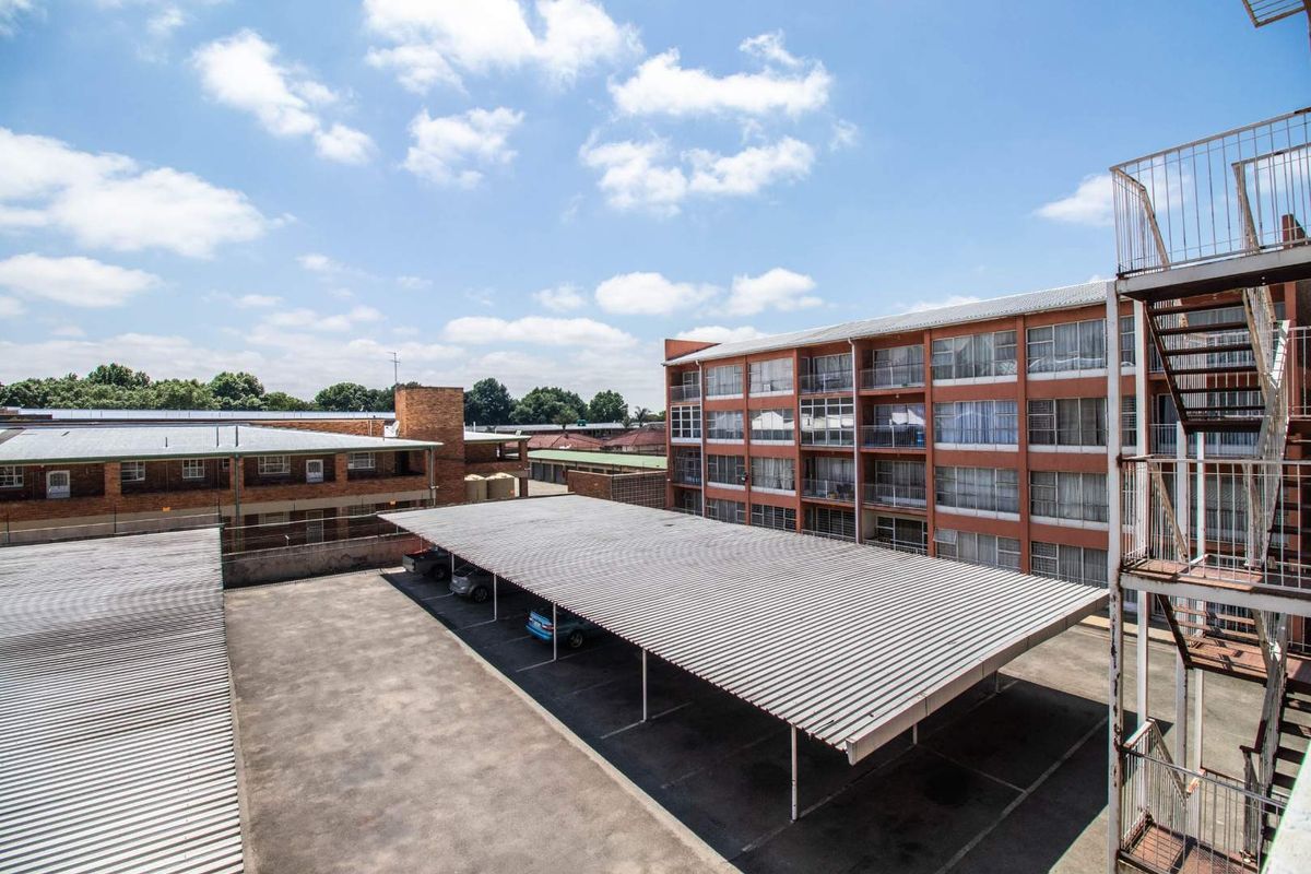 Elevated view of the apartment complex exterior, featuring covered parking bays and a multi-story residential building with external metal fire escape stairs.