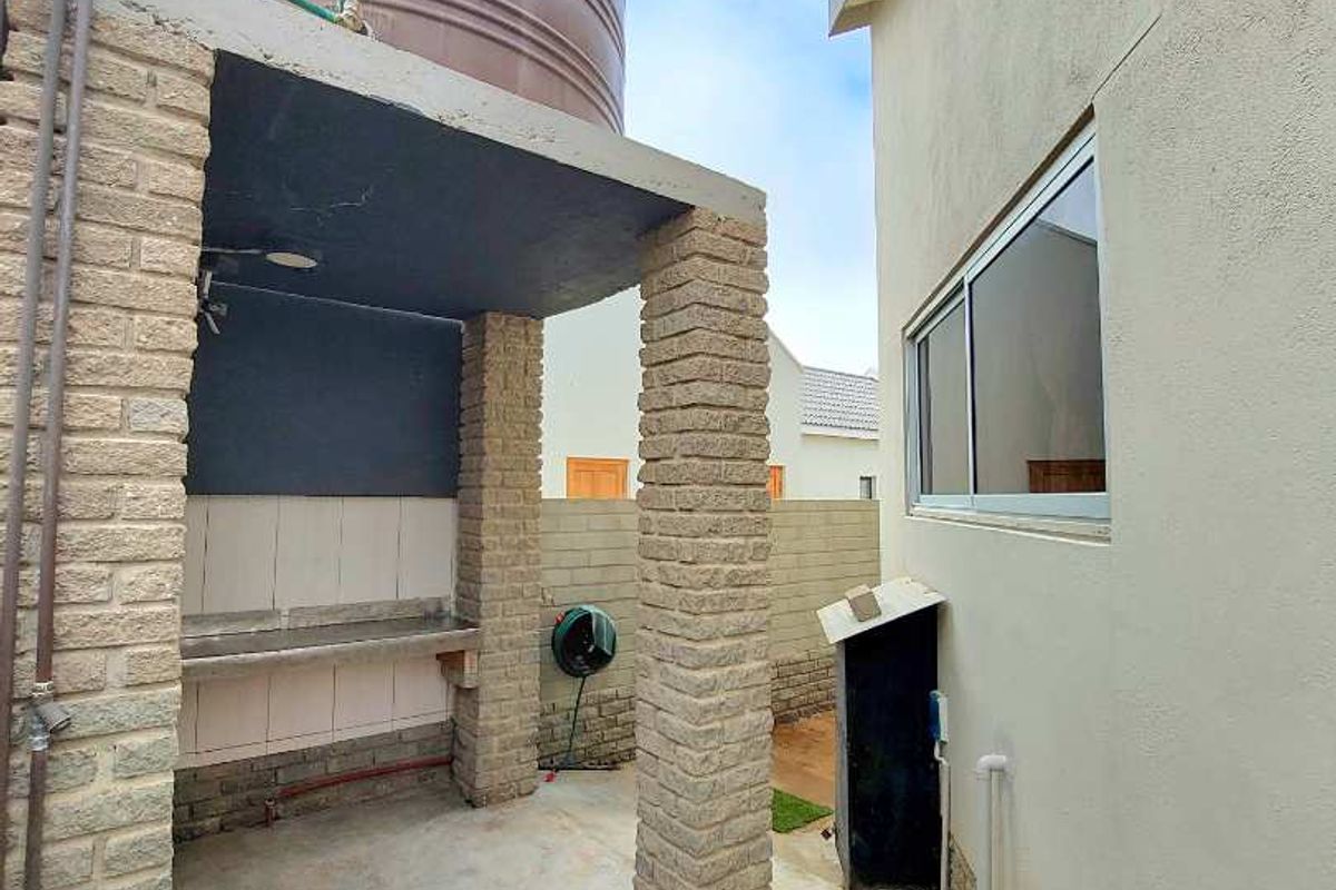 Outdoor area featuring a built-in brick braai structure, concrete flooring, and a large water storage tank positioned alongside the main house exterior.