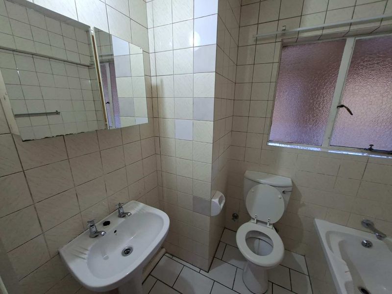 A functional bathroom featuring a pedestal basin, toilet, and bathtub with dated wall tiling and a frosted glass window.