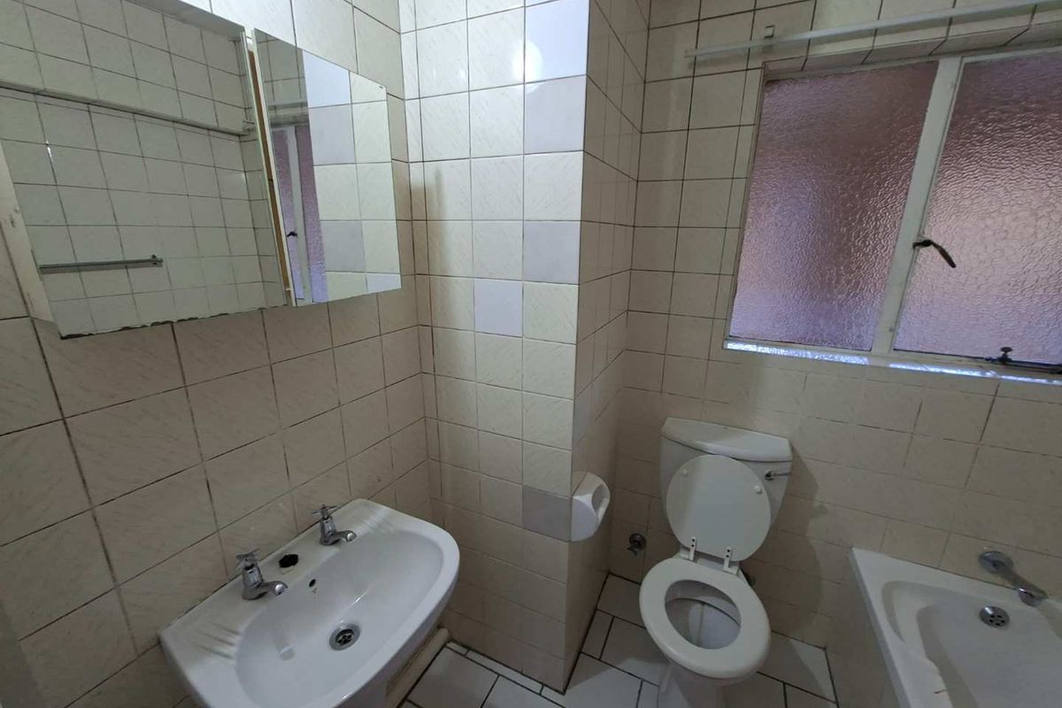 A functional bathroom featuring a pedestal basin, toilet, and bathtub with dated wall tiling and a frosted glass window.