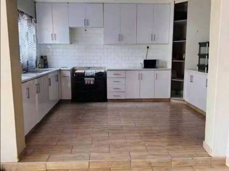 A clean, modern kitchen featuring white cabinetry, subway tile backsplash, built-in oven, and tiled flooring, presented in an open-plan layout.