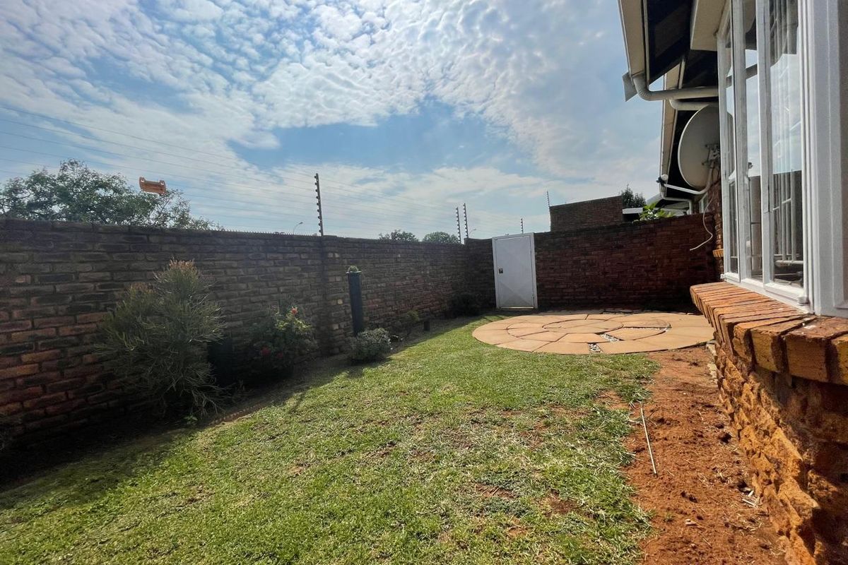 A private rear garden featuring a brick boundary wall with electric fencing, a small lawn area, and a circular paved patio.