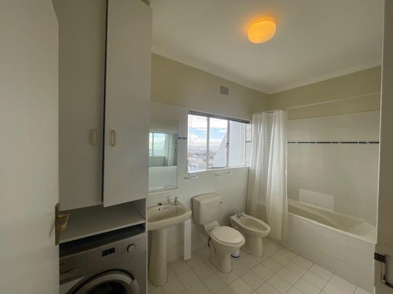 A functional bathroom featuring a pedestal basin, toilet, bidet, and bathtub with shower, including a built-in laundry cupboard for added utility.