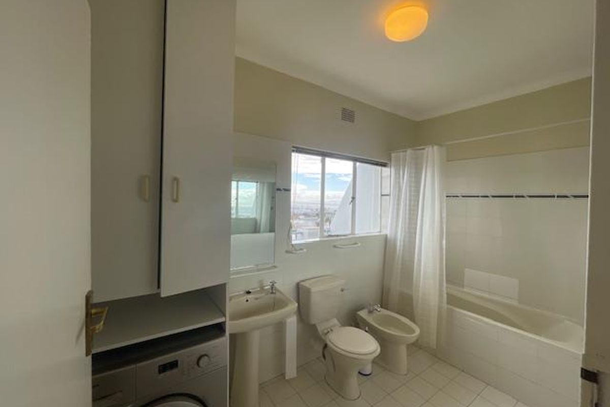 A functional bathroom featuring a pedestal basin, toilet, bidet, and bathtub with shower, including a built-in laundry cupboard for added utility.