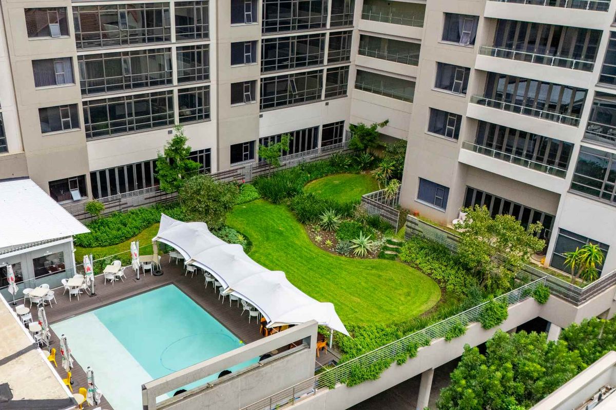 Aerial view of the apartment complex courtyard featuring a swimming pool, landscaped garden areas, and paved outdoor recreational space.