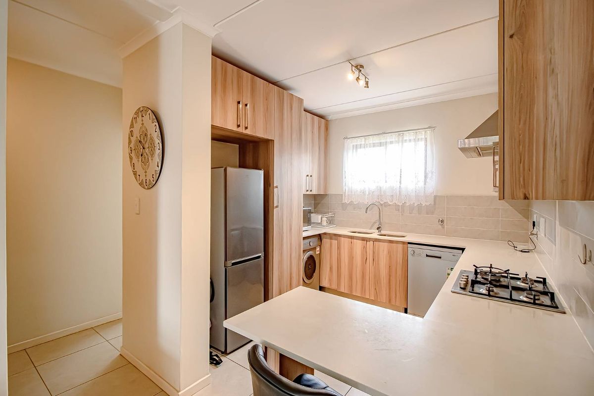 A functional kitchen featuring light wood cabinetry, stone-look countertops, a built-in gas hob, stainless steel extractor fan, and integrated space for appliances.
