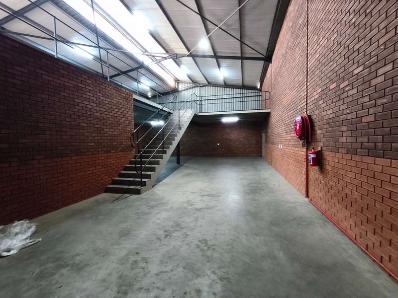 Spacious industrial warehouse unit featuring exposed brick walls, concrete flooring, a mezzanine level with metal staircase, and integrated fire safety equipment.