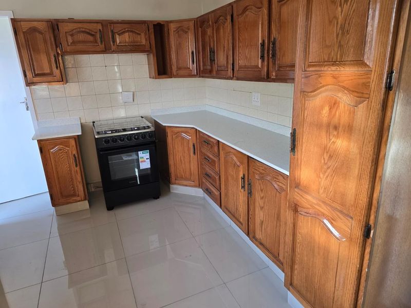 A functional kitchen featuring traditional wooden cabinetry, stone-look countertops, a tiled backsplash, and a freestanding oven, finished with neutral floor tiles.