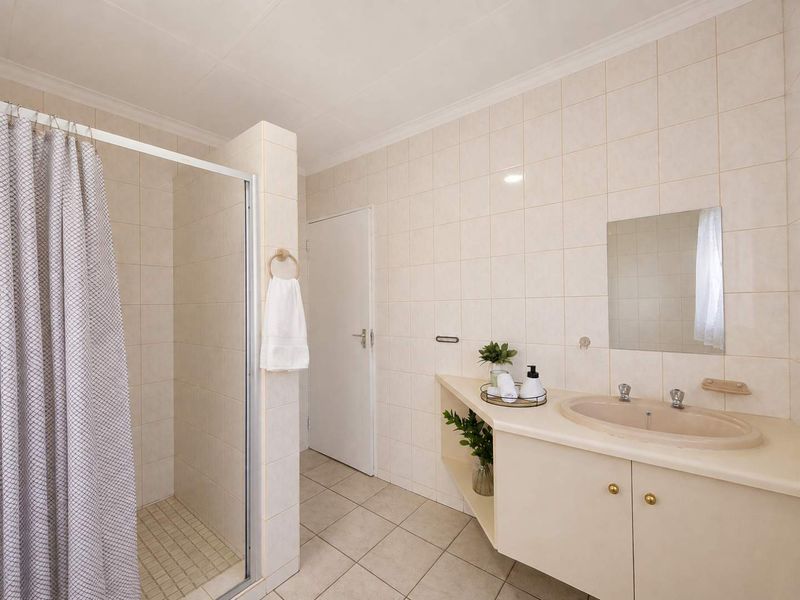 A functional bathroom featuring a shower enclosure, a built-in vanity with an integrated basin, and neutral wall tiling throughout.