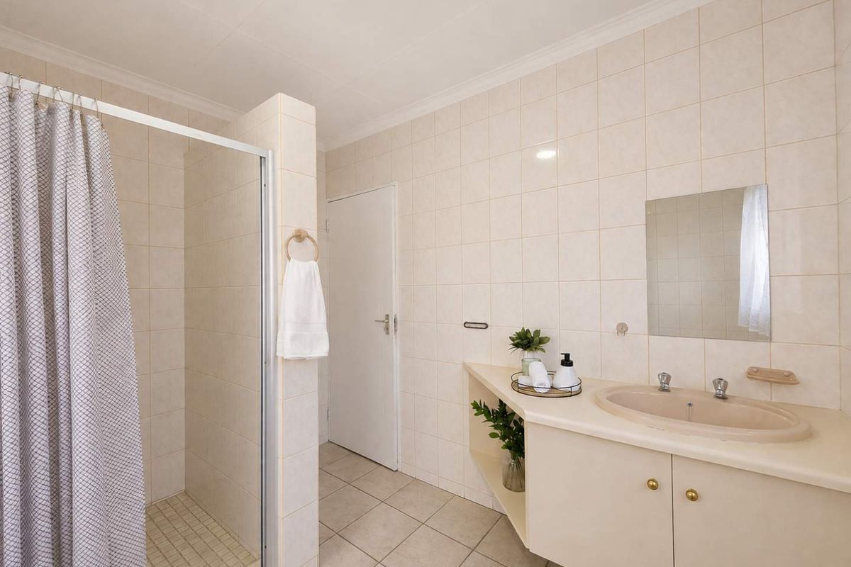 A functional bathroom featuring a shower enclosure, a built-in vanity with an integrated basin, and neutral wall tiling throughout.