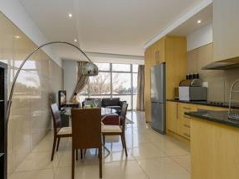 Modern open-plan living and kitchen area featuring tiled floors, sleek cabinetry, granite countertops, and large windows providing ample natural light.