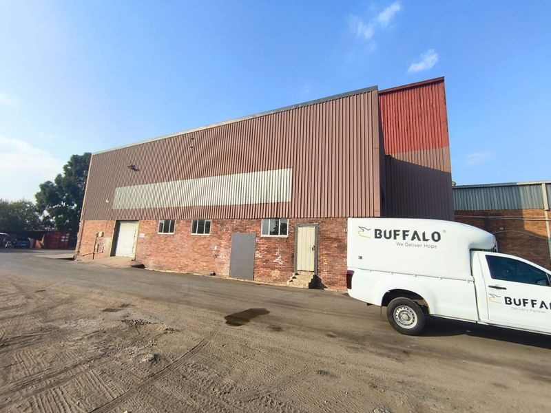 Industrial warehouse exterior featuring a combination of brick masonry and corrugated metal cladding with a large roller shutter door and pedestrian access.