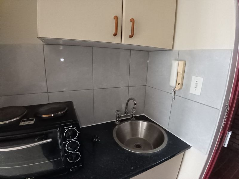 Compact kitchen area featuring upper and lower cabinetry, a stainless steel sink with mixer tap, and tiled splashback.
