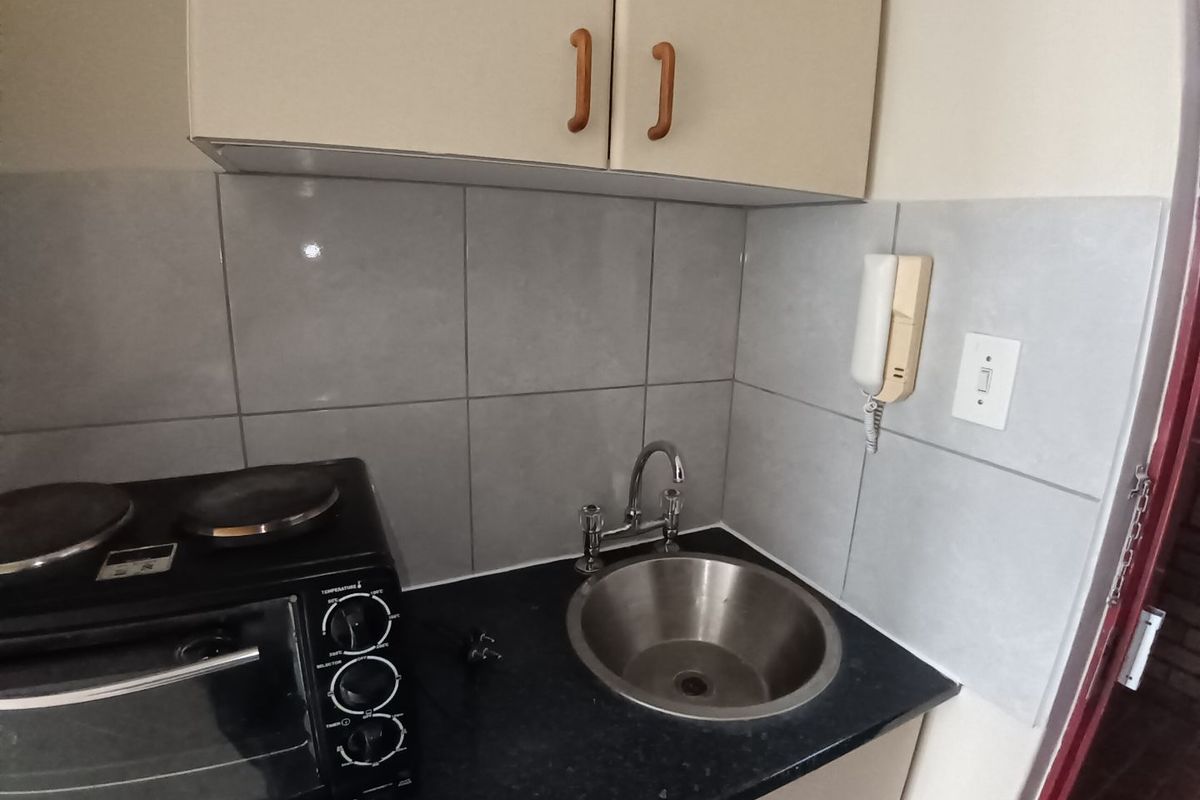 Compact kitchen area featuring upper and lower cabinetry, a stainless steel sink with mixer tap, and tiled splashback.