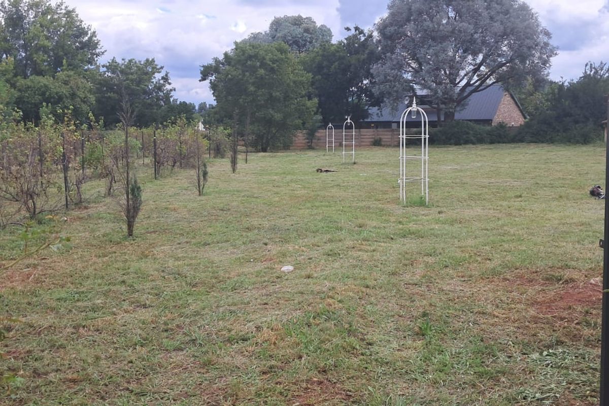 A view of a residential garden plot featuring brick entrance pillars, metal gates, and established garden trellises on a grassy lawn.