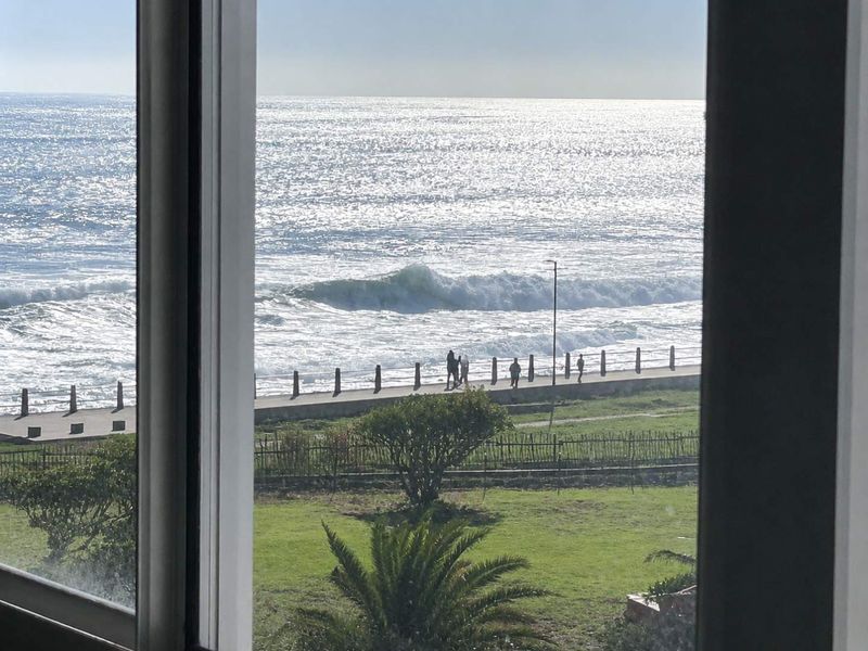 A clear, elevated view of the ocean and coastal promenade captured through a window.