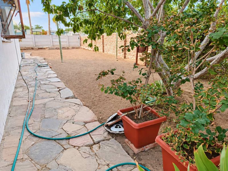 A rear garden area featuring a stone paved walkway alongside a brick and precast concrete boundary wall.