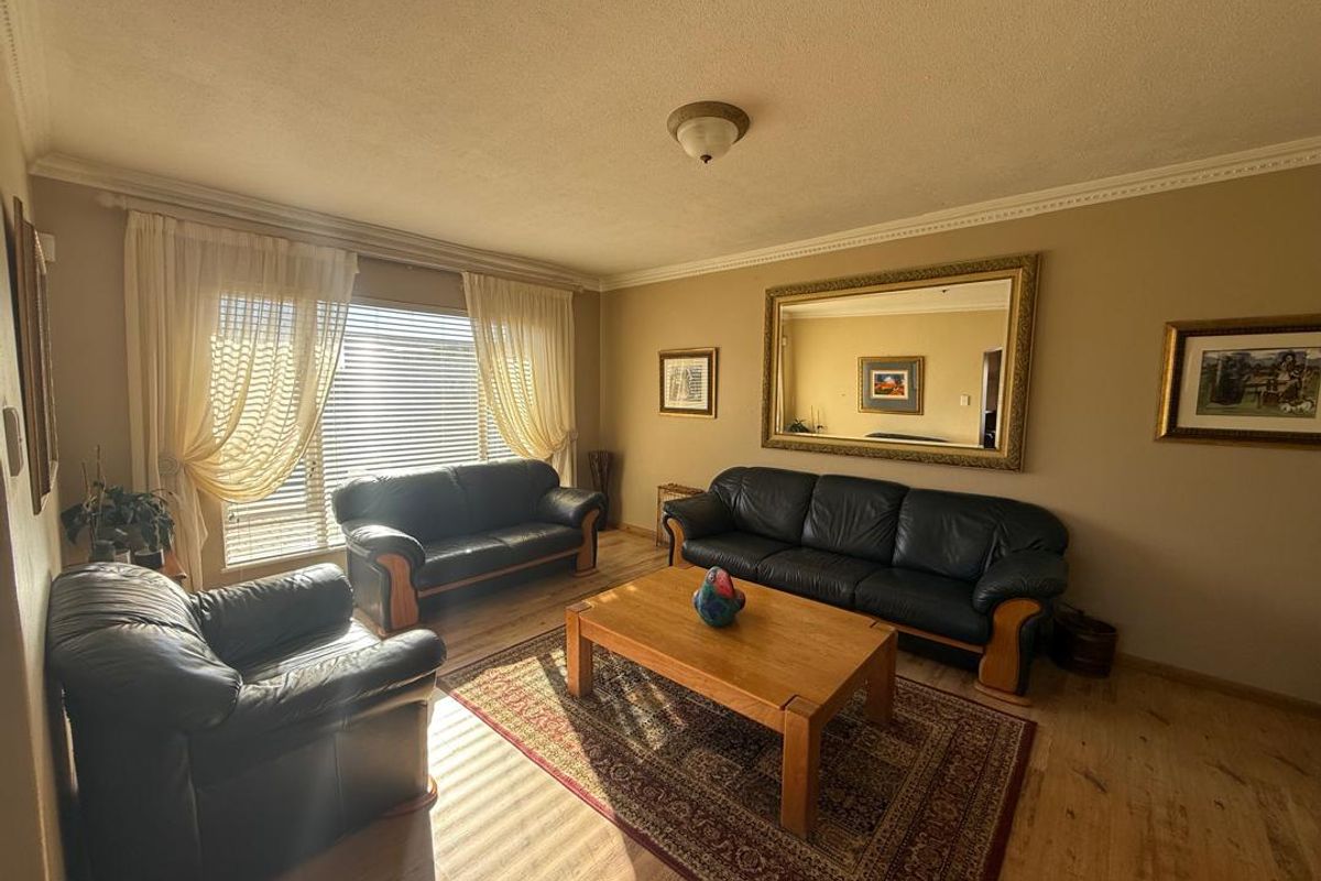 A spacious living room featuring wood-look flooring, large windows with natural light, and neutral wall tones, providing a comfortable and functional living space.