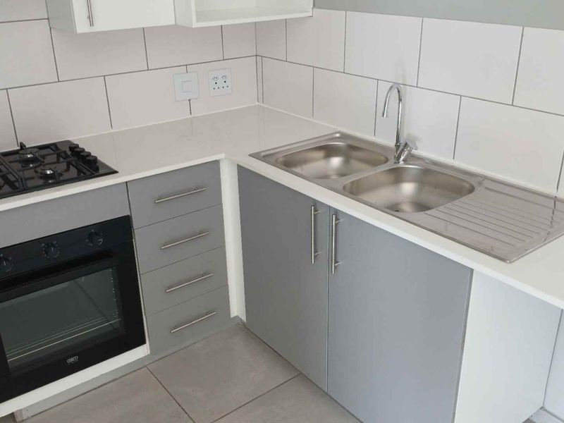 Modern kitchen featuring grey cabinetry, white stone countertops, a built-in oven, gas hob, and a double bowl stainless steel sink with tiled backsplash.