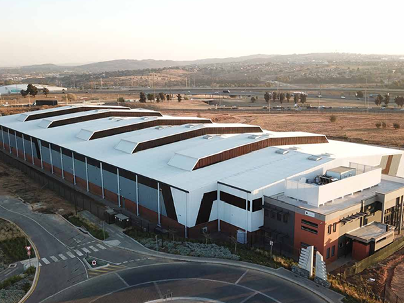 Aerial view of a modern industrial warehouse facility featuring a large span roof with skylights and an integrated office block.