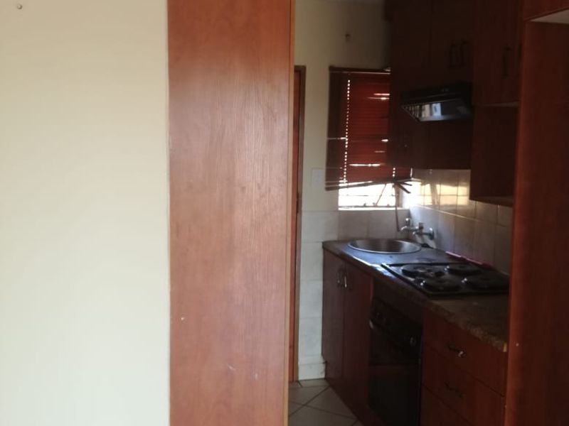 A compact, dated kitchen featuring wood-look cabinetry, built-in oven and hob, tiled backsplash, and tiled flooring.