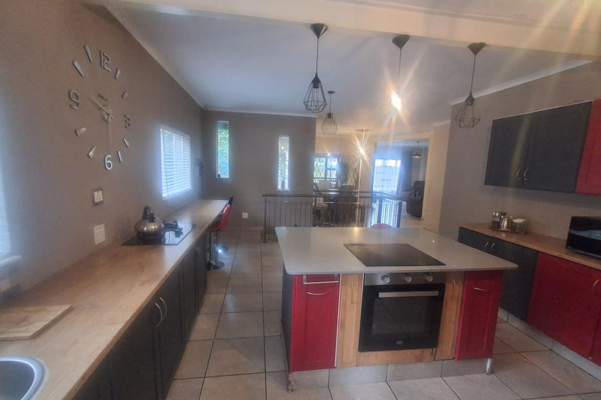 Spacious kitchen featuring a central island with built-in oven and cooktop, ample cabinetry, and tiled flooring, flowing into the adjacent living area.