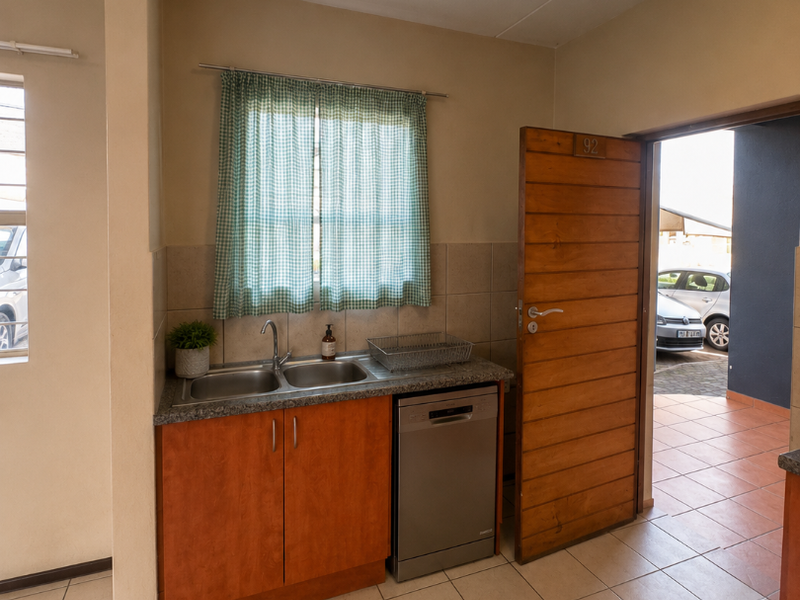 Compact kitchen area featuring built-in cabinetry, a double basin sink, and an integrated dishwasher, with direct access to an outdoor patio area.