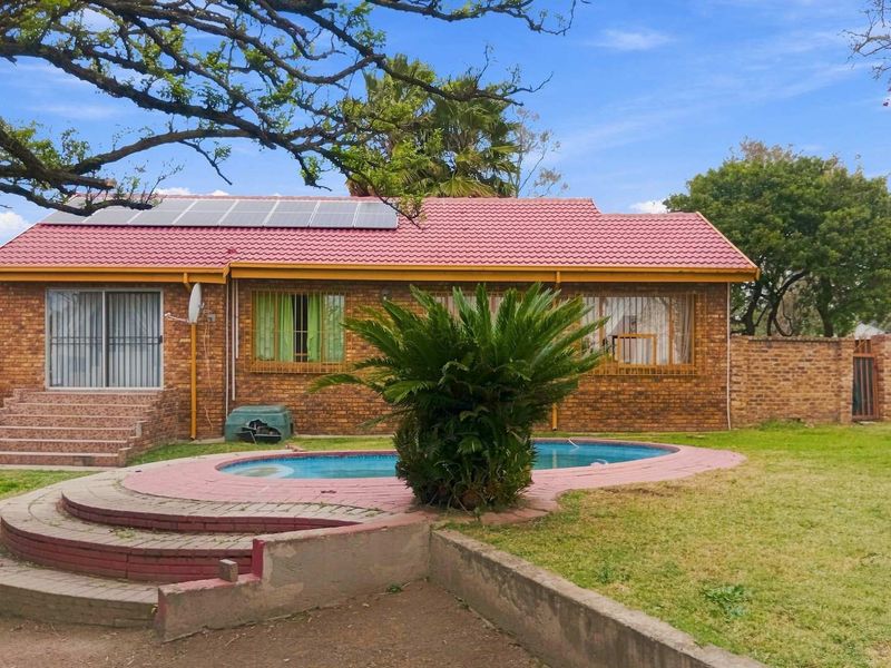Rear view of a brick house featuring a swimming pool, paved patio area, and roof-mounted solar panels set within a private garden.